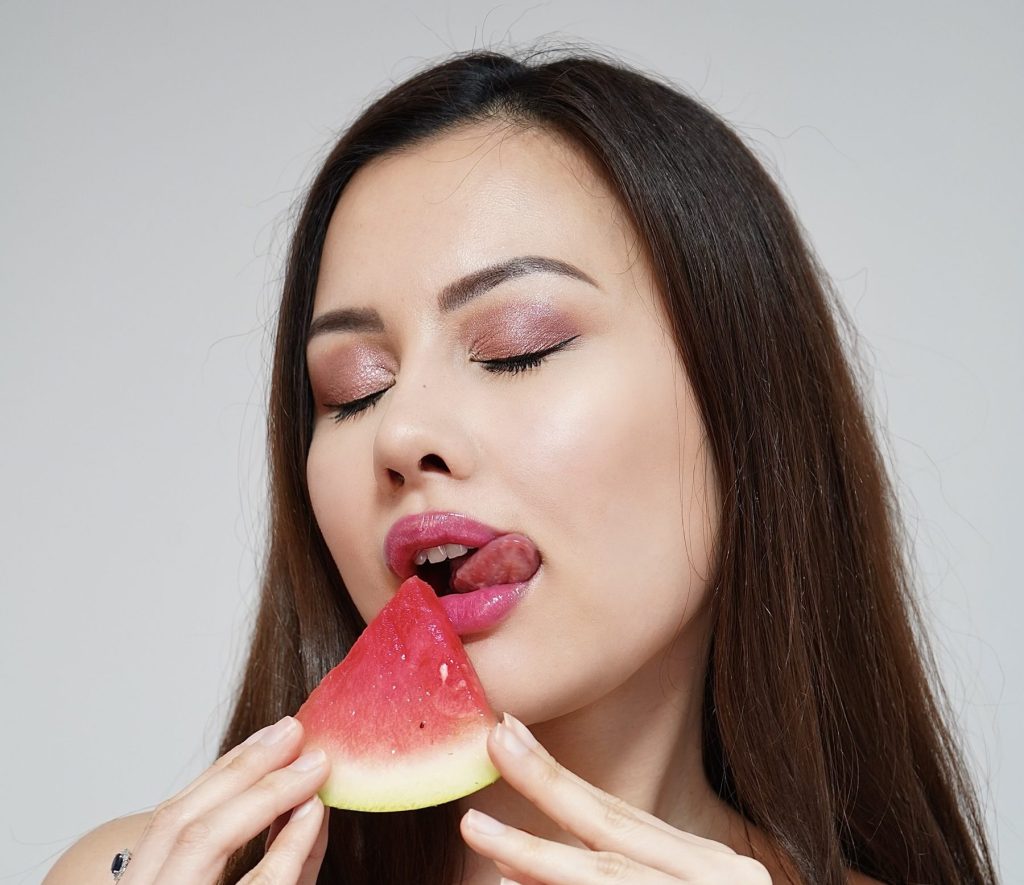 Lip Care Routine with Lip Oils: Hydrate, Nourish, and Shine! Photo - A beautiful woman with perfectly hydrated lips licking a watermelon
