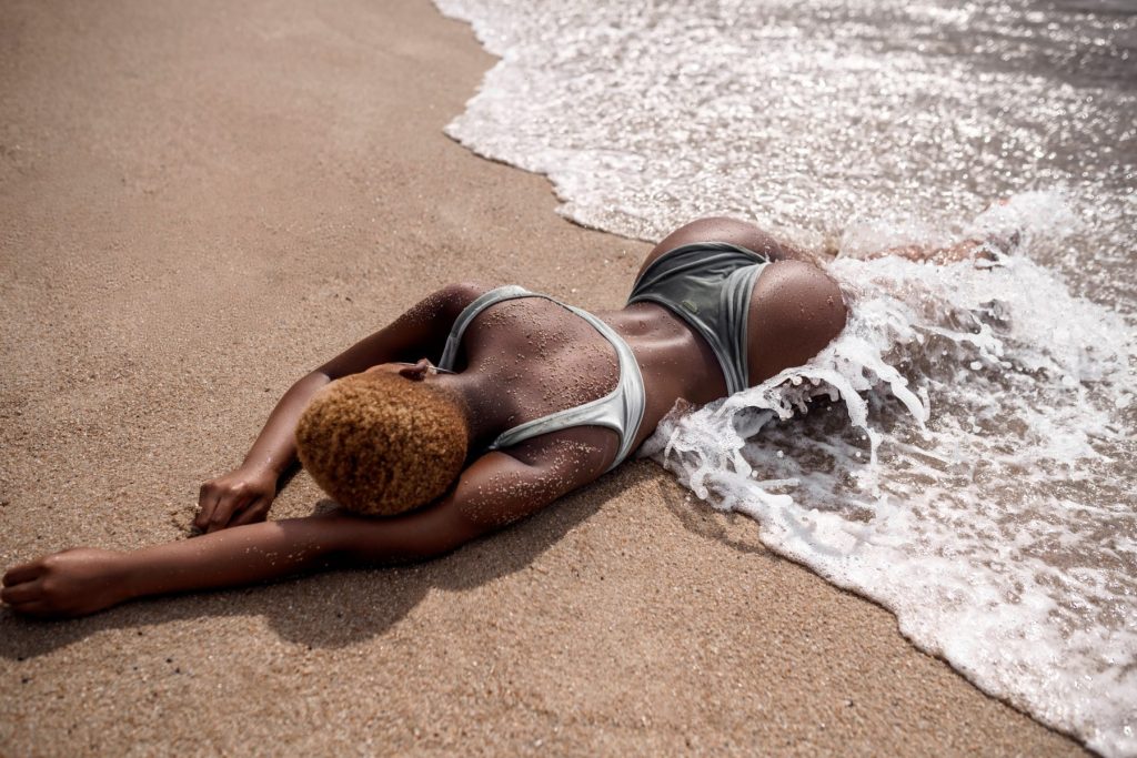 How to Naturally Enhance Your Curves Without Surgery: The Rise of Injectable Body Contouring A woman looking fabulous at the beach in a bikini. Laying down as the waves hit her body after getting injectable body contouring