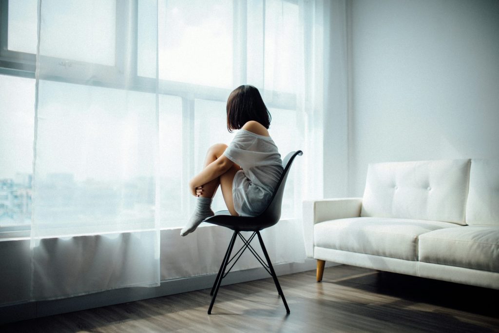 How Stress Affects Your Skin & How to Fix It: Expert Skincare Tips That Work Photo - A sad woman looking out the window thinking about How Stress Affects Your Skin